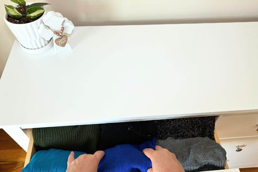 My hands arranging clothes in an open dresser drawer.